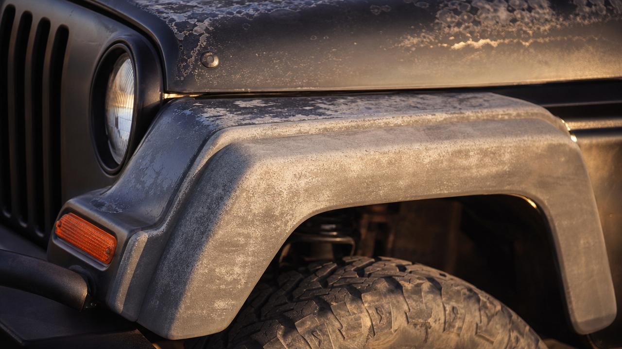 Close-up of a faded Jeep Wrangler fender with oxidized gray plastic and UV damage under warm sunlight